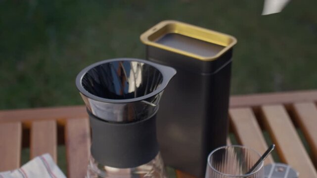 Hand placing paper filter into coffee dripper on glass carafe on wooden table outdoors. Concept of manual brewing home beverage preparation and coffee routine.