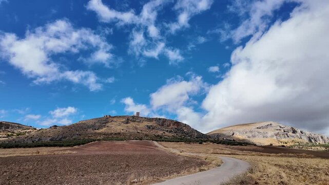Static real-time shot of Castillo de la Estrella in Spain, featuring clouds moving across the sky and grass swaying in the wind on a sunny day.