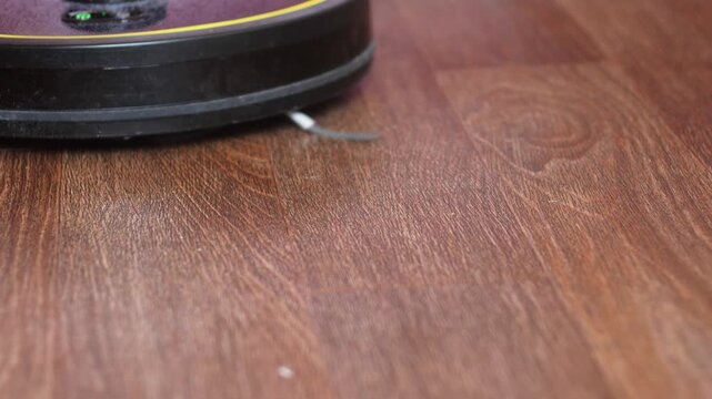 Modern robotic vacuum cleaner performing automated cleaning on wooden laminate floor. Smart household appliance for maintaining cleanliness and order at home