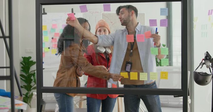 Diverse group of startup team engaging in brainstorming session, using sticky notes on glass wall to organize ideas, plan next steps. Creativity and collaborative spirit of modern entrepreneurial team