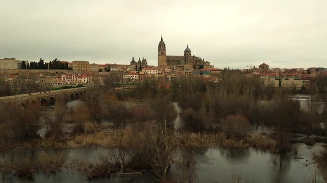 Aerial panoramic view of Salamanca featuring the cathedral complex and the Roman Bridge over the Tormes River. Historic architecture and skyline in western Spain.