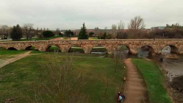 Drone aerial view of the ancient Roman stone bridge crossing the Tormes River in Salamanca, Spain. Historic landmark and architectural heritage captured from above.
