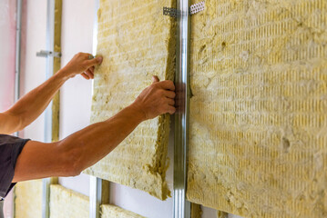 Obraz premium Worker insulating a room wall with mineral rock wool thermal insulation.