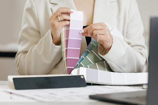 Female designer selecting paint colors from swatches in office setting with online client for interior creative design on notebook