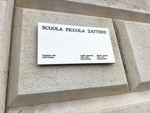 Scuola Piccola Zattere sign mounted on a textured wall in Venice, Italy, displaying opening hours and contact information