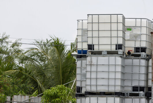 white ibc container in outdoor stock yard of factory, white plastic chemical tanks. The containers are piled on top of each other.