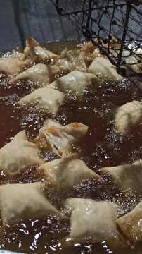 Siomay goreng immersed in hot cooking oil, undergoing rapid thermal conduction and moisture evaporation, resulting in a golden-brown crust and a crisp exterior texture.