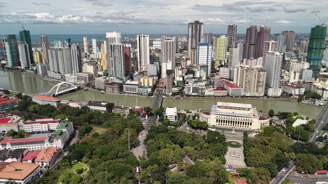 Elevated aerial view from Intramuros shows Pasig River crossed by white arch bridge with neoclassical post office building and dense modern Manila skyline rising toward Manila Bay