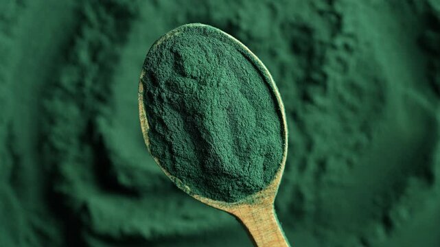 Heap of green spirulina algae powder in a wooden spoon, top view on green spirulina powder background rotates. Dietary supplement to improve health. Seaweed superfood concept. Healthy food