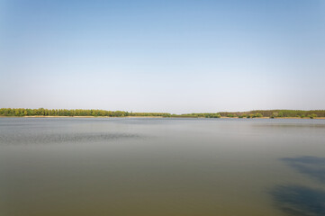 The still waters of a lake mirror the sky under a clear blue horizon.