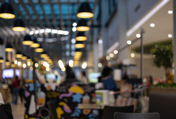 Fototapeta premium blurred interior of a modern industrial cafe and food court with rows of hanging warm pendant lights and colorful wall art for urban lifestyle background.