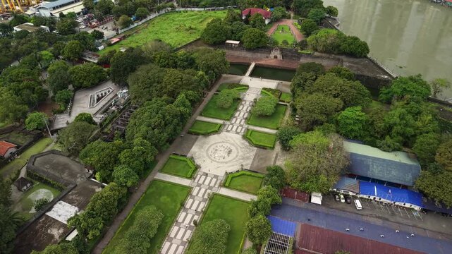 Aerial top-down view reveals Fort Santiago formal gardens with symmetrical geometric green lawns and central stone medallion with cross-shaped pathways surrounded by fortress walls and tropical trees