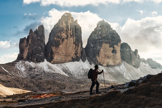 Male hiker stands on trail admiring the massive Tre Cime mountain and blue sky in Dolomites, Italy