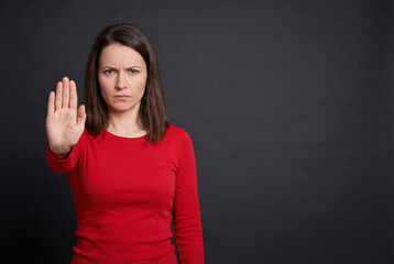 Fototapeta premium Frustrated Woman Showing Stop Hand Gesture Against Dark Gray Background, Expressing Disagreement or Warning