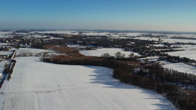Winter aerial of rural town and snowy fields under blue sky, contryside landscape 4k.