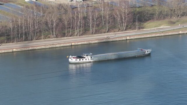 25 february 2026, Genk, Belgium. Aerial,Drone Shot of Cargo Barge Passing Industrial Warehouse, Solar Power Plant and Power Substation, Inland Shipping and Sustainable Energy Logistics. supply chain, 