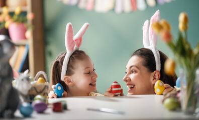 Fototapeta premium Happy Mother and Daughter Wearing Bunny Ears, Decorating Easter Eggs, Smiling Together at Home