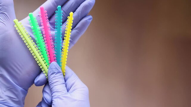 Close view of dental professional holding orthodontic tools and multicolored elastic ligature bands used for braces adjustment. Clinical procedure highlights modern orthodontic treatment and oral care