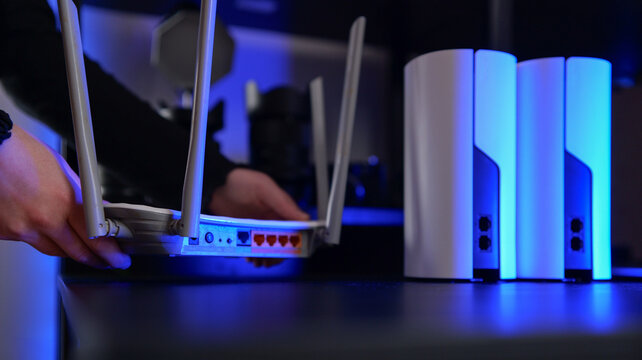Hands setting up a modern Wi-Fi router and mesh system with blue ambient lighting