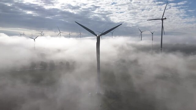 Turbines turning above a layer of fog, generating clean and renewable electrical energy. Drone View