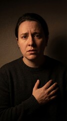 Obraz premium A poignant studio portrait of an individual, conveying a sense of deep concern, touching their chest with a hand, the muted tones emphasize the subject's emotional state.