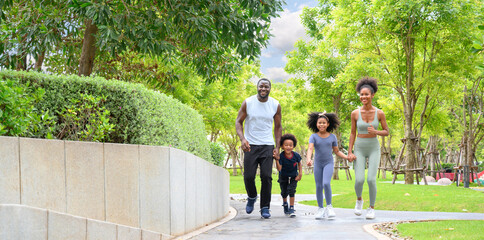 Happy African American family in sportswear running in public park. father carrying son with mother and daughter. Family exercising together concept.