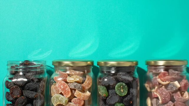 Jars filled with various dried fruits and candies sit on a teal background.