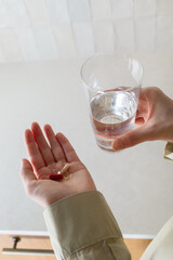 Woman taking vitamin pills with glass of water in modern kitchen as daily routine. Medication nutrition supplement capsules for healthy lifestyle and medicine self care.