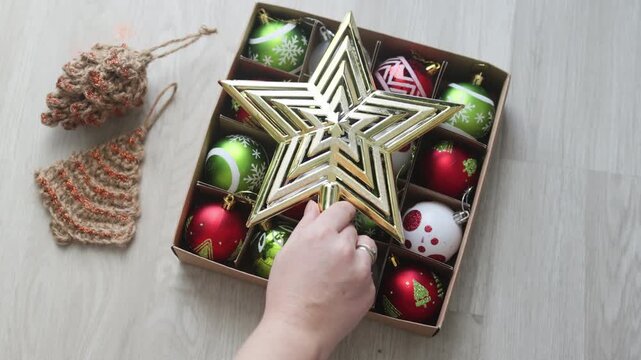 Holiday Storage features hand placing gold star in box with ornaments. Efficient Holiday Storage ensures safe keeping of festive tree topper and colorful baubles.