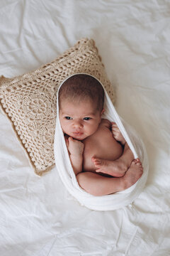 Newborn baby wrapped in soft cloth resting on textured pillow on bed