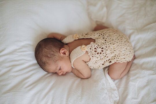 Newborn baby sleeping peacefully on soft white bedding in cozy handmade outfit
