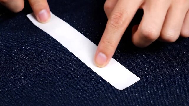 Hands applying white tape on a textured, dark blue fabric. Close-up shot with focus