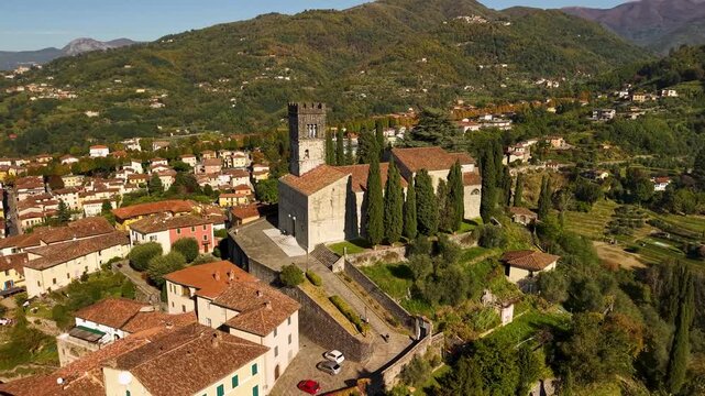 Barga cathedral aerial 4k view with Apuan Alps mountains in Italy. Cinematic drone orbit of Duomo di San Cristoforo on hill with medieval old town. Garfagnana highlands autumn scenery. Tuscany landsca