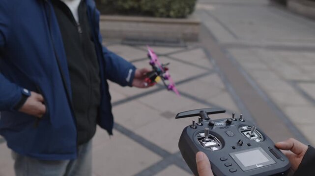 Adult pilot holds a small fpv racing quadcopter and remote controller, preparing the miniature drone for outdoor flight in a park setting, preflight check underway