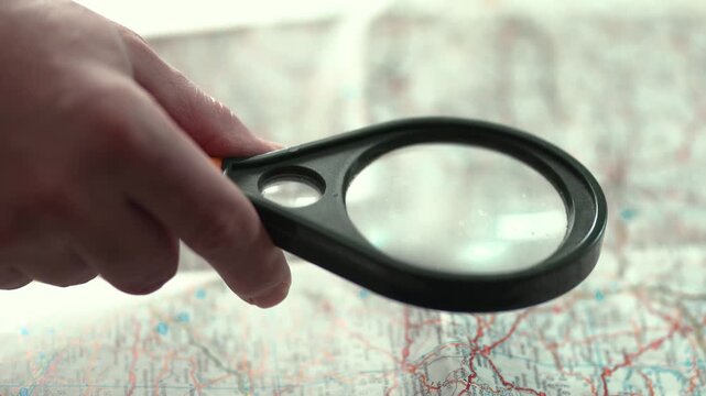 Hand holding magnifying glass over map for research and travel planning.