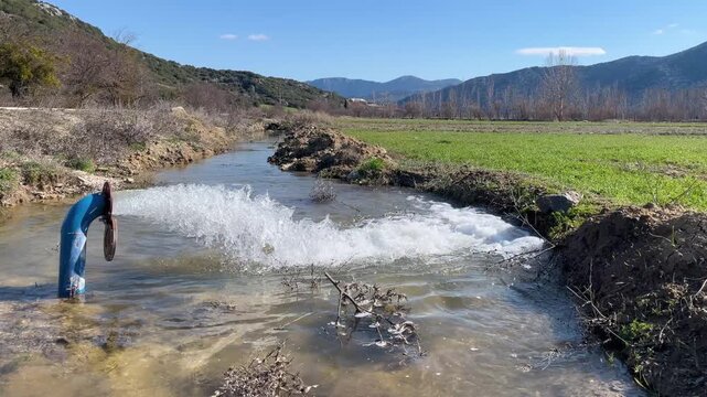 A natural flow created by water flowing under pressure from an agricultural irrigation pipe on a large plot of land with mountain views. Modern agriculture, water resources, and rural life.