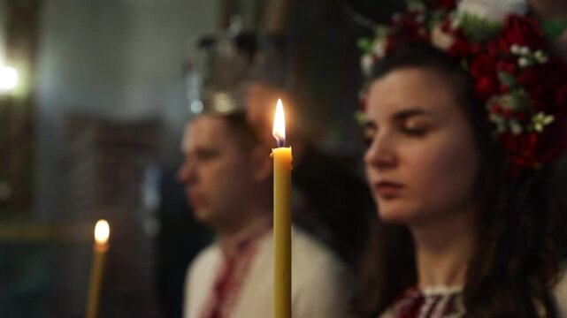 The bride and groom in traditional costume hold lit candles during a church wedding. Ukraine.