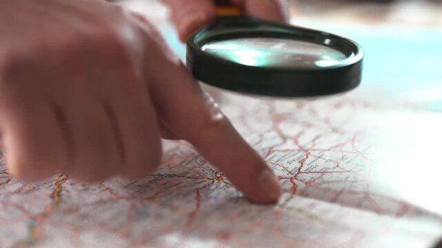 Hand holding magnifying glass over map for research and travel planning.