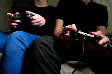 Two gamers competing in a video game at home, hands holding gamepads in a dark room, focus on controllers. Friends playing console games, close-up of hands with joysticks, indoor leisure activity. © Dina Luk