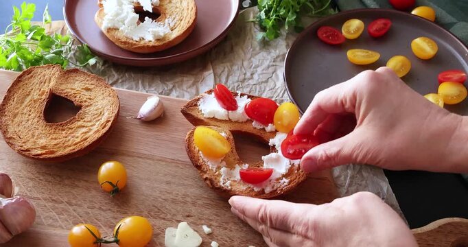 Anonymous person prepares round bruschetta with creamy goat cheese and cherry tomatoes in kitchen. Italian cuisine, high-quality farm-grown ingredients.