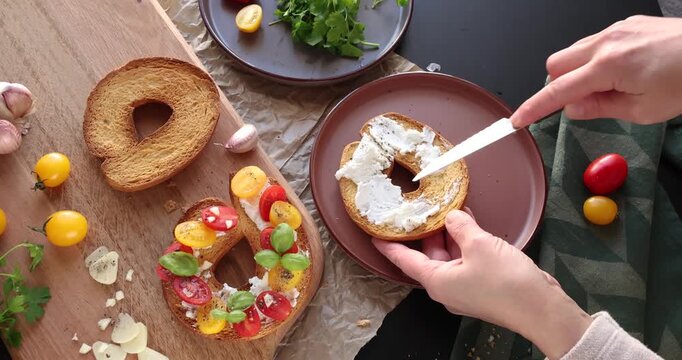 Anonymous person prepares round bruschetta with creamy goat cheese and cherry tomatoes in kitchen. Italian cuisine, high-quality farm-grown ingredients.