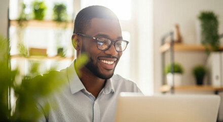 Naklejka premium Cheerful black man with glasses smiling while working in a bright home office