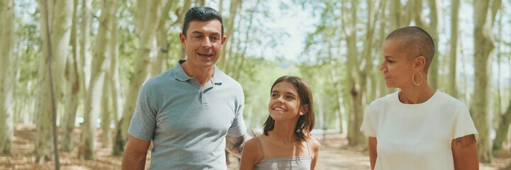 Fototapeta premium Happy family, mom dad and daughter, spend time together talking and walking in the city park. Panoramic