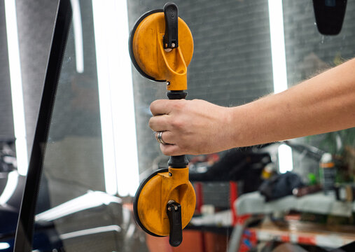 Automobile special workers replacing windscreen or windshield of a car in auto service station garage. Glass of the car, removed with the help of professional suction cups. The process of car repair.