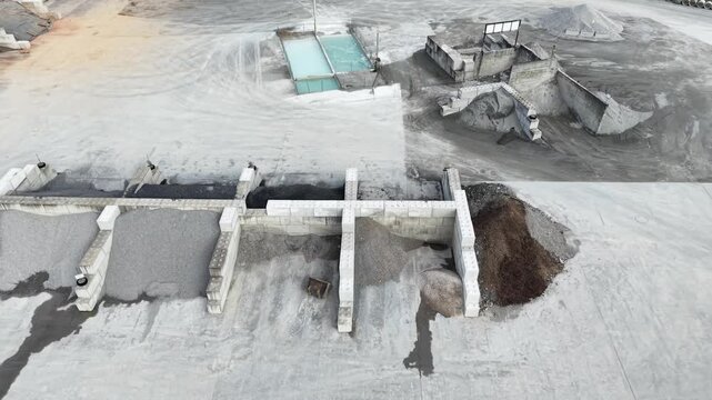 Lateral drone movement across organized sand compartments in industrial yard with highway traffic in background, ending near large storage silo for cement or aggregates, construction supply chain conc