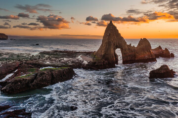 Rock arch at sunset on Martins Beach along the Pacific Coast Highway in California with ocean waves and glowing golden sky over the Pacific Ocean