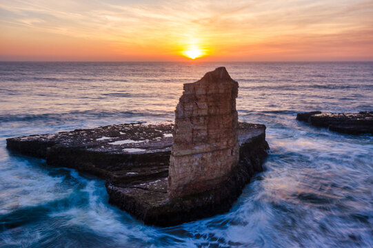 Rock formation at sunset on Four Mile Beach in Santa Cruz California with ocean waves swirling around coastal cliffs under a golden sky