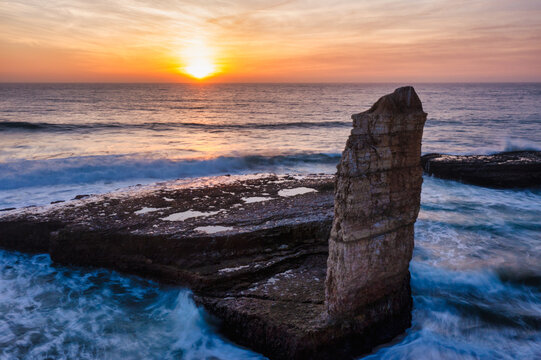 Rock formation at sunset on Four Mile Beach in Santa Cruz California with ocean waves swirling around coastal cliffs under a golden sky