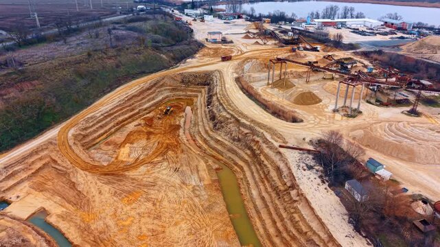 Wide aerial shot of open pit sand quarry operation. Panoramic view of excavation site with machinery and lake background