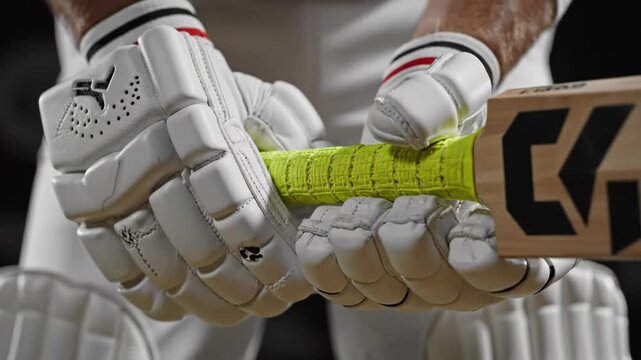 Cricketer gripping bat tightly during preparation for a match, showcasing the focus and intensity required in sports. Ideal for articles on cricket training, sports gear, or outdoor activities.